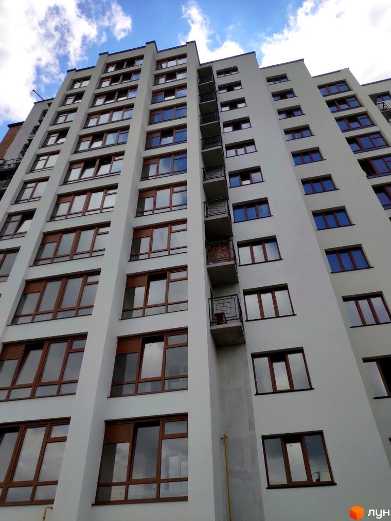 Зовнішній вигляд багатоповерхового будинку за адресою вул. Плоска, 23/1. Фасад будівлі світлого кольору з великими вікнами.