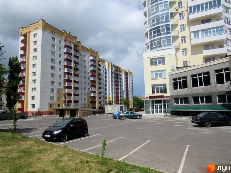 Новобудова на просп. Миру, 63а, б, в з білими та жовтими фасадами, червоними балконами. Поруч парковка з автомобілями та зелені насадження.