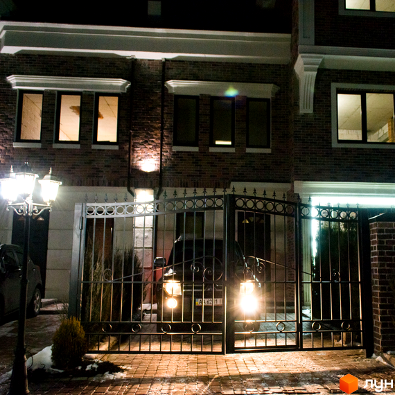Таунхауси Liverpool House з цегляним фасадом та кованими воротами. Перед будинком розташована підсвічена алея та парковка.