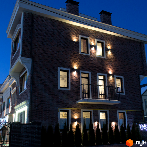 Таунхауси Liverpool House з цегляним фасадом та підсвіткою вночі. Перед будинком висаджені туї та встановлена огорожа.