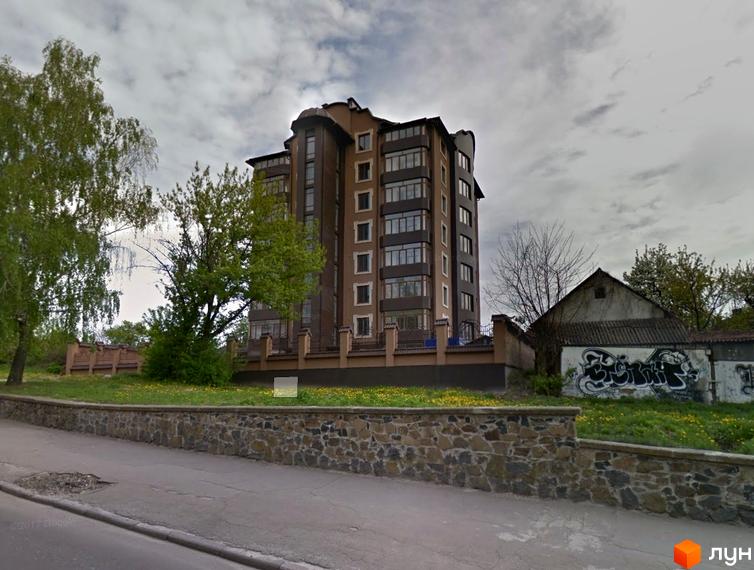 Житловий комплекс на вулиці Князя Володимира, 28б, з багатоповерховим будинком коричневого кольору та великими вікнами. Перед ним зелена галявина і кам'яна огорожа.