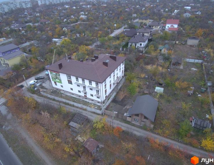 Зображення триповерхового будинку з коричневим дахом, Житлового комплексу „Міські сади“. Навколо будинку дерева та інші будівлі.