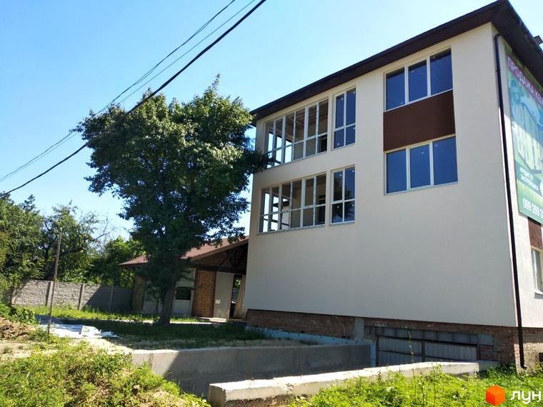 Зображення фасаду будівлі Клубний будинок „Міські сади“ з великими вікнами та прилеглою територією з деревами та зеленню.