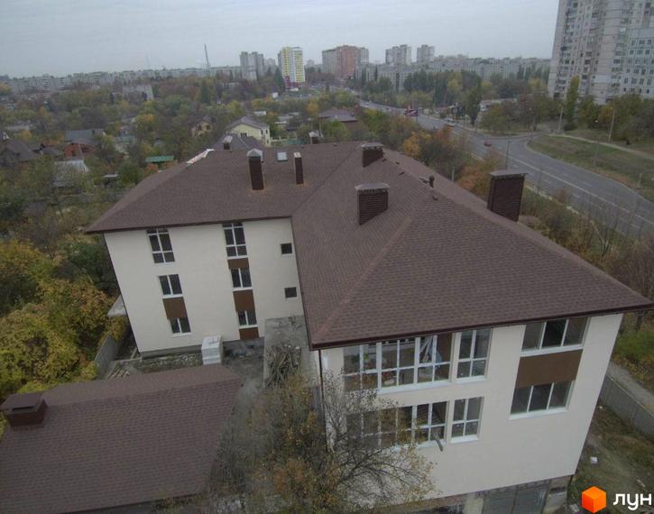 Зображення фасаду будівлі Клубний будинок „Міські сади“ з коричневим дахом та світлими стінами. Навколо будівлі видно дерева та інші будівлі.