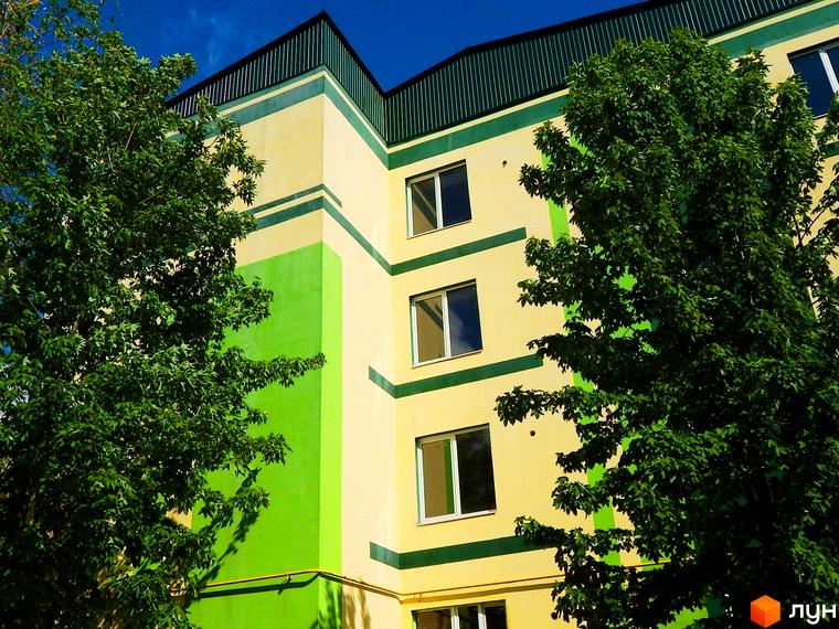 Новобудова ЖК Усадьба з яскравим фасадом жовто-зелених кольорів. Навколо будівлі ростуть зелені дерева.