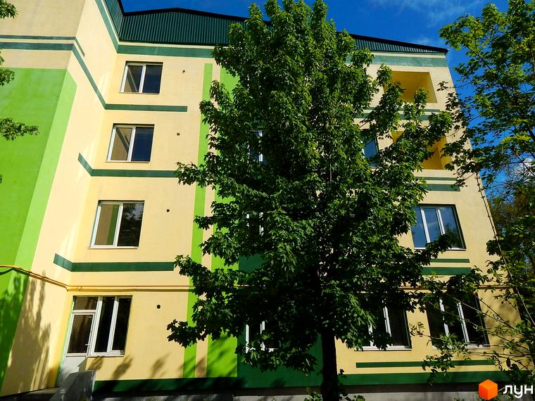 Житловий комплекс Усадьба. Зовнішній вигляд багатоповерхового будинку з жовто-зеленим фасадом та балконами. Навколо зелені дерева.