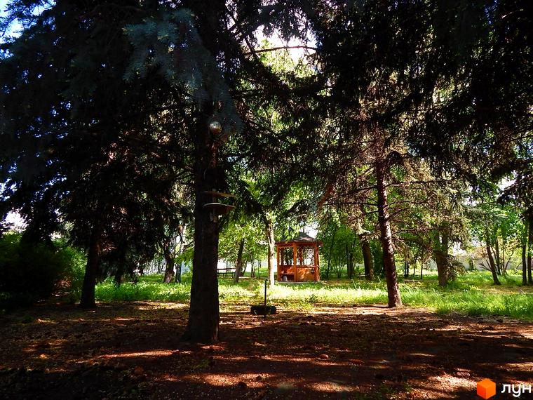 Житловий комплекс Усадьба в оточенні дерев. Зелена прибудинкова територія з альтанкою та місцем для відпочинку.