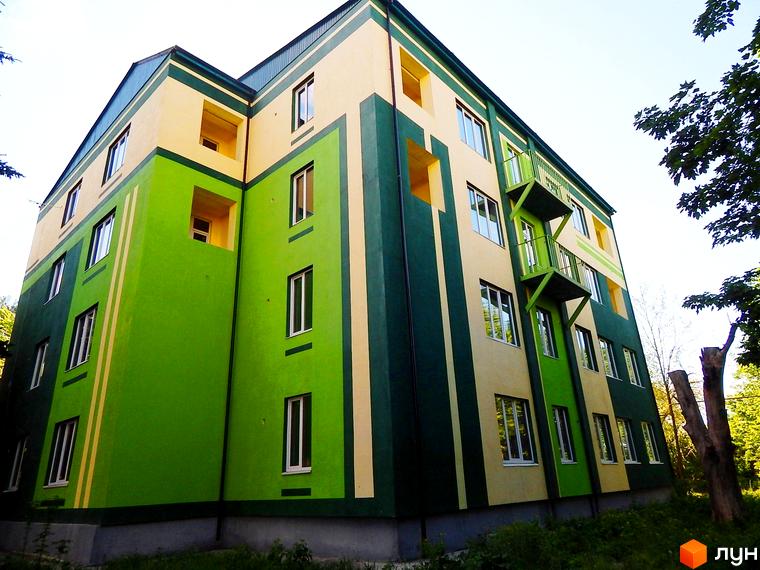 Житловий комплекс Усадьба: багатоповерхова будівля з зеленим та жовтим фасадом, вікнами та балконами. Навколо видно зелень та дерева.