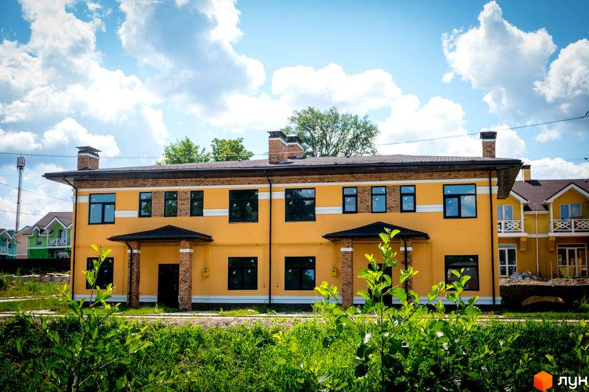 Зовнішній вигляд двоповерхового будинку в Котеджному містечку Sun City. Житло з жовтими стінами та чорними вікнами, зелена прибудинкова територія.