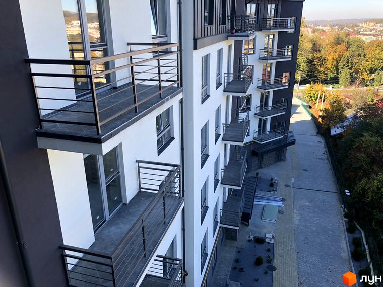 Зовнішній вигляд новобудови на вулиці Черемшини, 29, з балконами та вікнами. Прибудинкова територія з бруківкою та деревами.