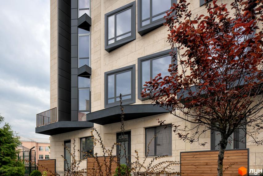 Фасад Таунхаусів Struetinsky з світлою облицюванням, темними віконними рамами та вертикальними елементами. На передньому плані дерево з червоним листям.