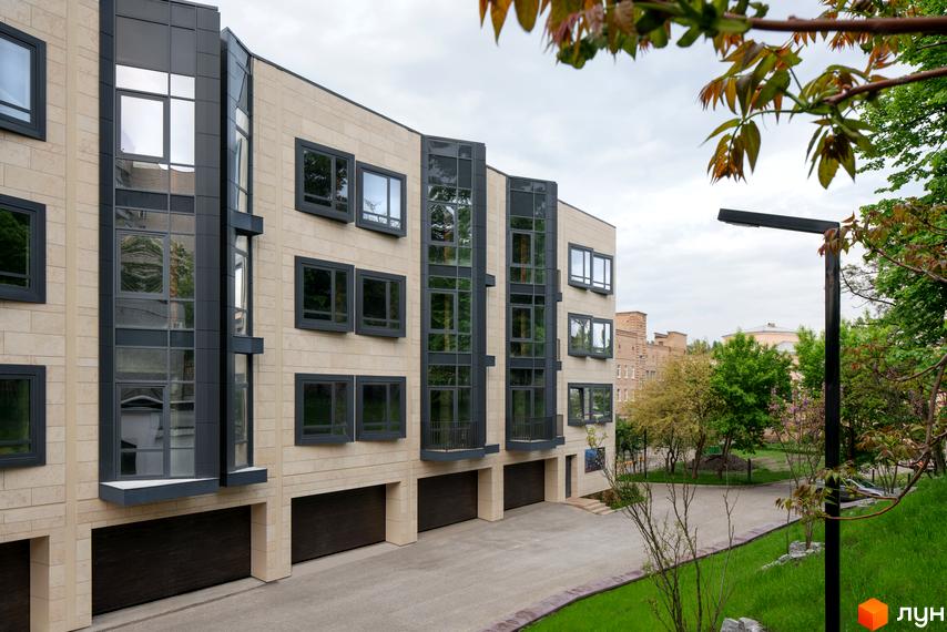 Зовнішній вигляд таунхаусів Struetinsky: світлий фасад, великі темні вікна, скляні секції та гаражні ворота. Доріжка та зелена зона навколо будинку.