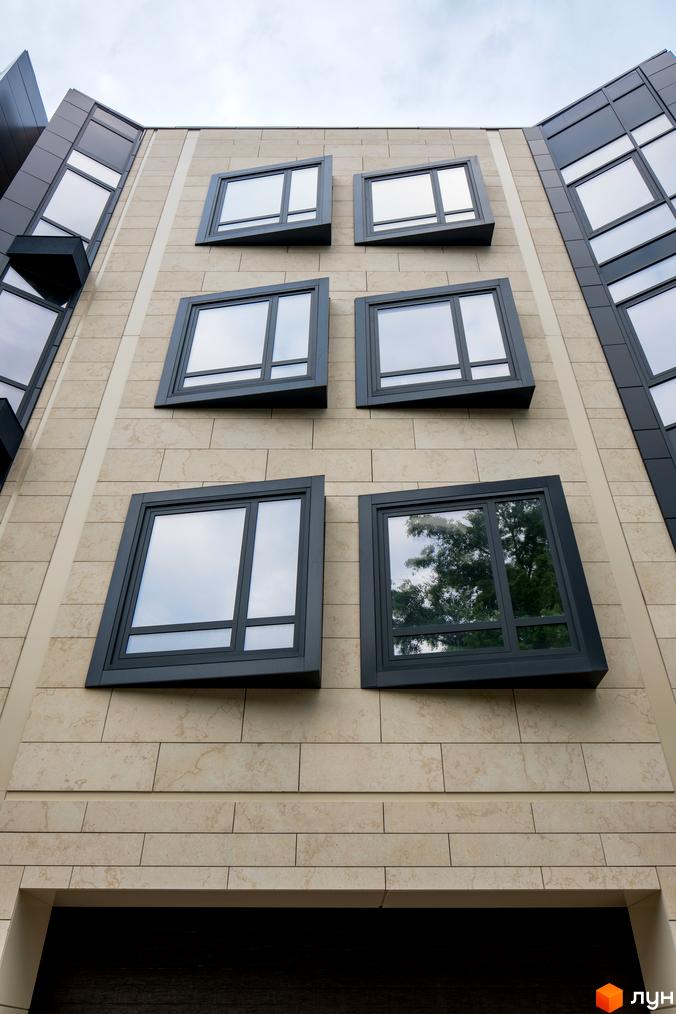 Фасад Таунхаусів Struetinsky, облицьований світлою плиткою, з темними вікнами, що мають незвичайну геометричну форму. Видно частину бічних фасадів.