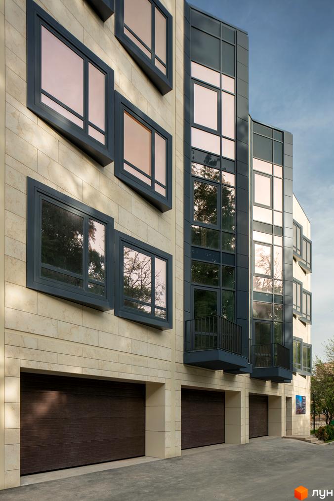Фасад житлового комплексу Struetinsky з великими вікнами та гаражними воротами. Зовнішній вигляд новобудови з кам'яним оздобленням та темними елементами.