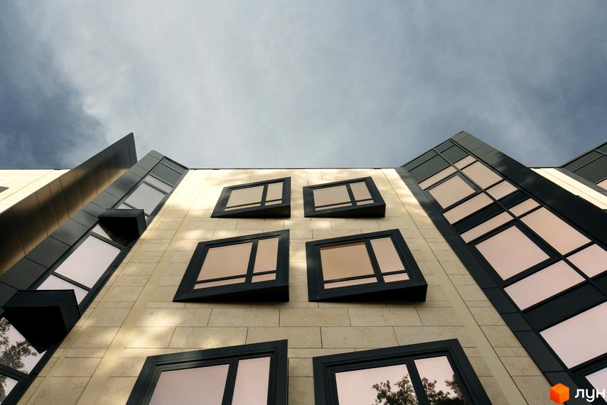 Фасад Таунхаусів „Struetinsky“ з бежевою облицюванням та темними віконними рамами. Будівля має виразні гострі кути та асиметричні вікна.