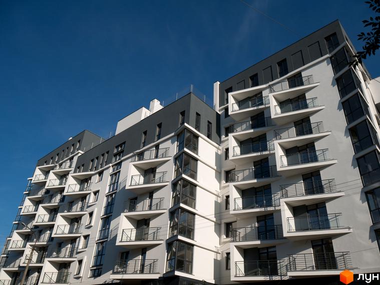 Зовнішній вигляд новобудови ЖК 360 з численними балконами та панорамними вікнами на фоні блакитного неба. Будинок має біло-сіре оздоблення фасаду.