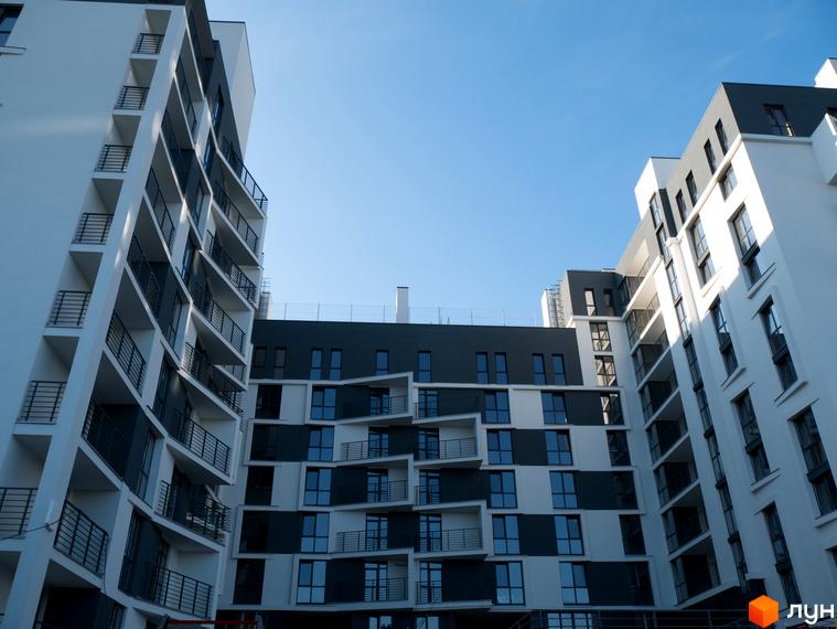 Зовнішній вигляд житлового комплексу 360 з білими та темними фасадами, численними балконами та панорамними вікнами. Комплекс розташований на фоні блакитного неба.