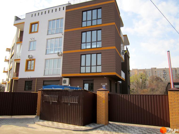 Зовнішній вигляд будинку Клубний будинок „Чорногорія“. Багатоповерховий будинок з панорамними вікнами та балконами. Територія огороджена коричневим парканом.