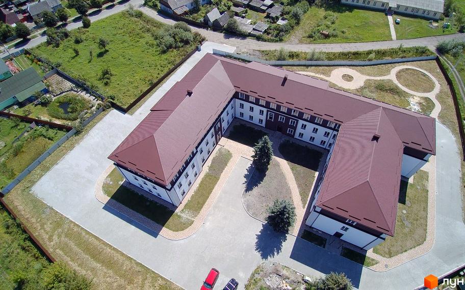 Житловий комплекс Княжий, вид зверху на будівлю з коричневим дахом та білими стінами, навколо доглянута прибудинкова територія з зеленими насадженнями та парковкою.