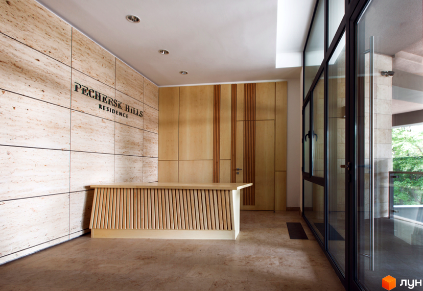 Інтер'єр холу ЖК Pechersk Hills Residence з оздобленням з натурального каменю та дерев'яними панелями. Стійка ресепшн з дерев'яними рейками.