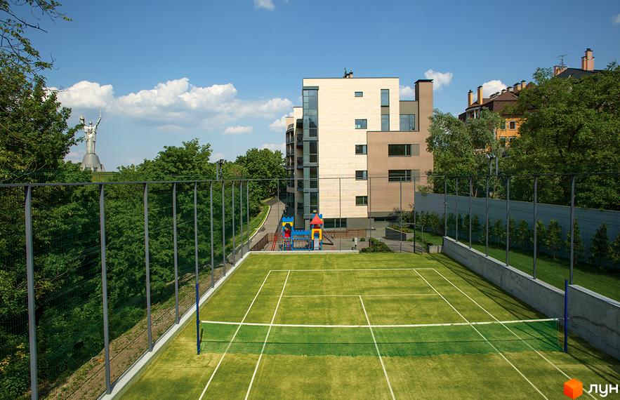 Житловий комплекс Pechersk Hills Residence з тенісним кортом та дитячим майданчиком. Багатоповерховий будинок з панорамними вікнами на тлі зелених насаджень та блакитного неба.