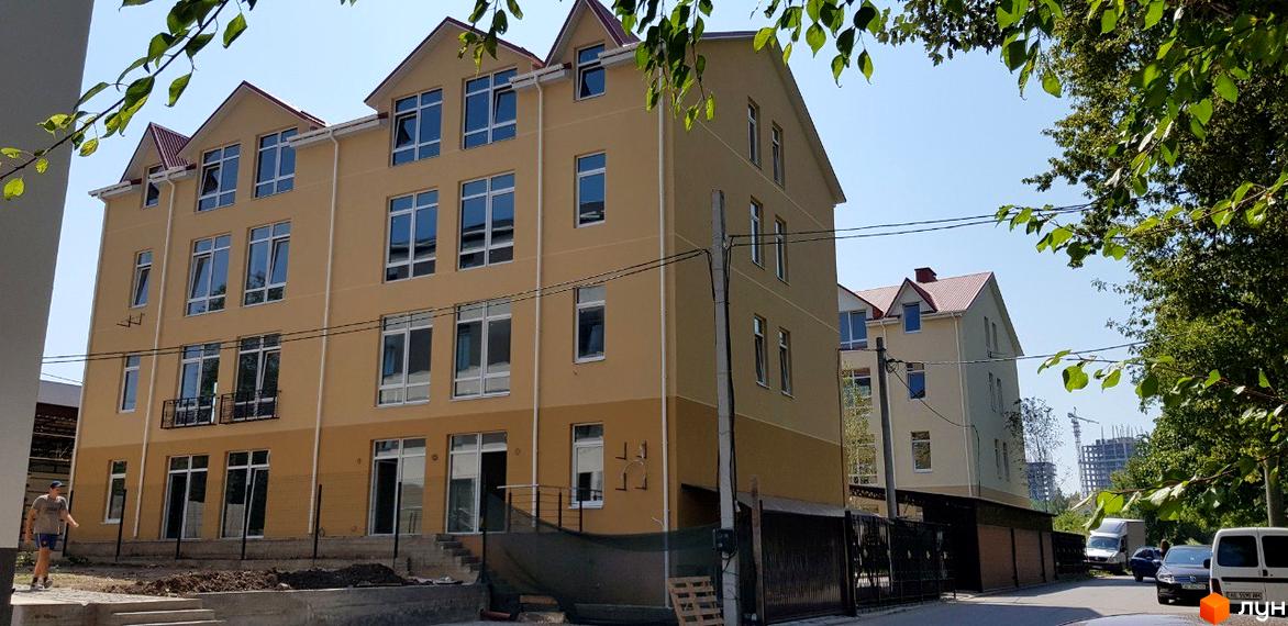 Клубний будинок „Ліон“ з жовтим фасадом та червоним дахом, поруч дорога з автомобілями та зелені дерева.