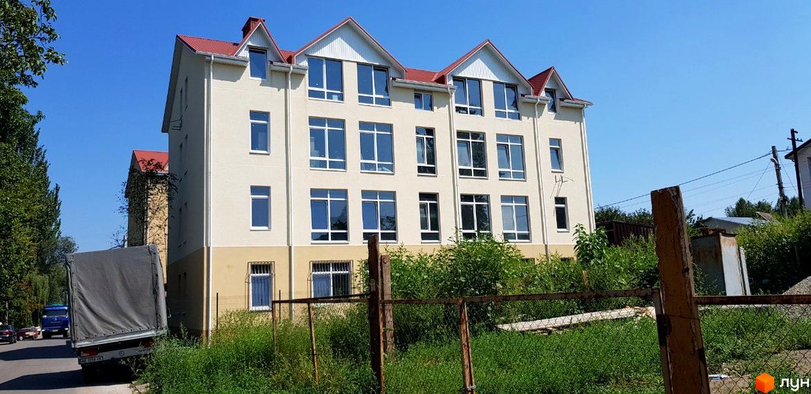 Клубний будинок „Ліон“ – це чотириповерхова новобудова світло-бежевого кольору з червоним дахом та великими вікнами. Навколо будинку зелена територія з деревами та кущами.