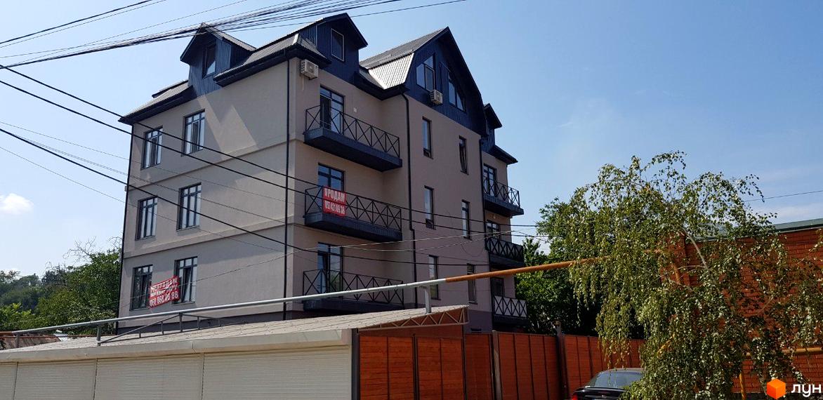 Клубний будинок „Женева“ з балконами та вікнами на тлі блакитного неба. На фасаді будинку розміщено оголошення про продаж.