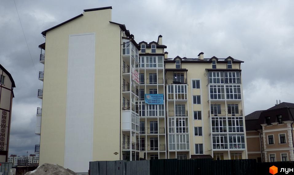 Багатоповерховий будинок з балконами та скляними вікнами. На фасаді будівлі розміщені рекламні банери. Похмура погода.