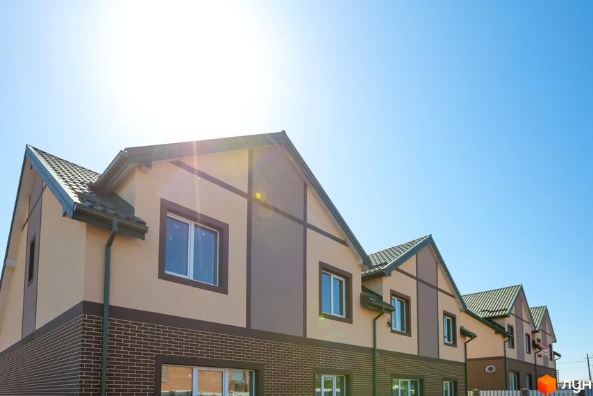 Котеджне містечко КМ Панич. Фасад будинку з цегляною нижньою частиною та світлими стінами, прикрашений темними балками. Зелений дах та вікна.