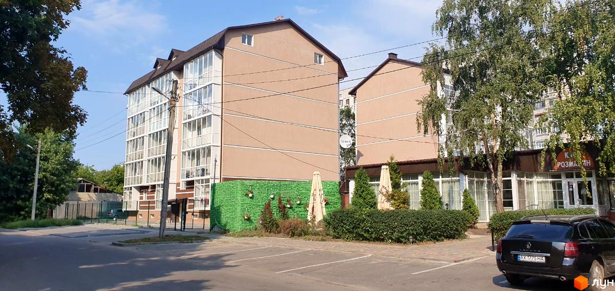 Новобудова ЖК Фесенківський з панорамними вікнами та зеленою прибудинковою територією з парасольками.