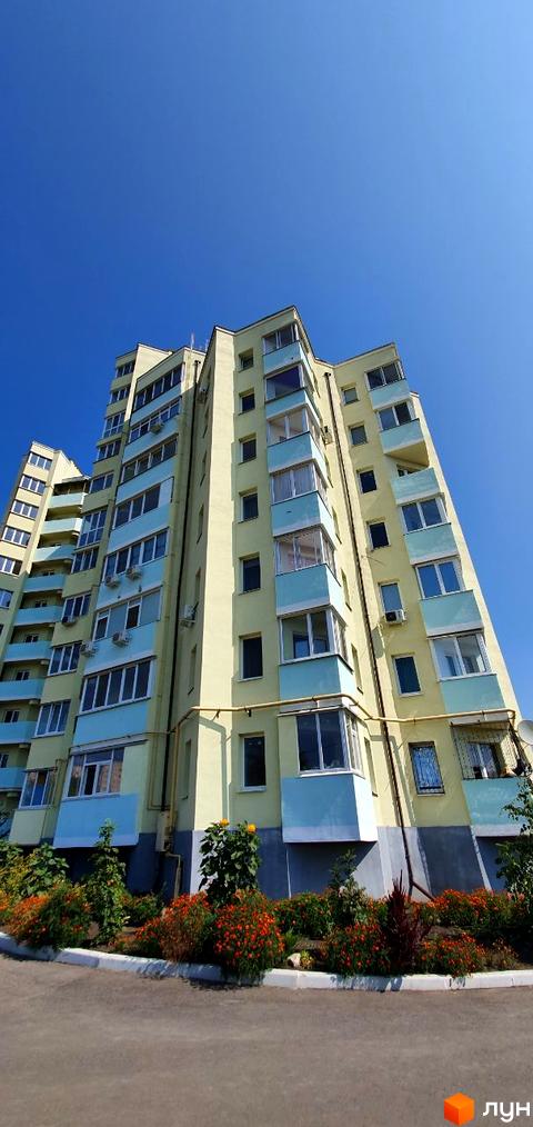 Світло-жовтий багатоповерховий житловий комплекс з блакитними балконами на вулиці Людвіга Свободи (біля №20). Навколо будинку висаджені квіти та зелені насадження.