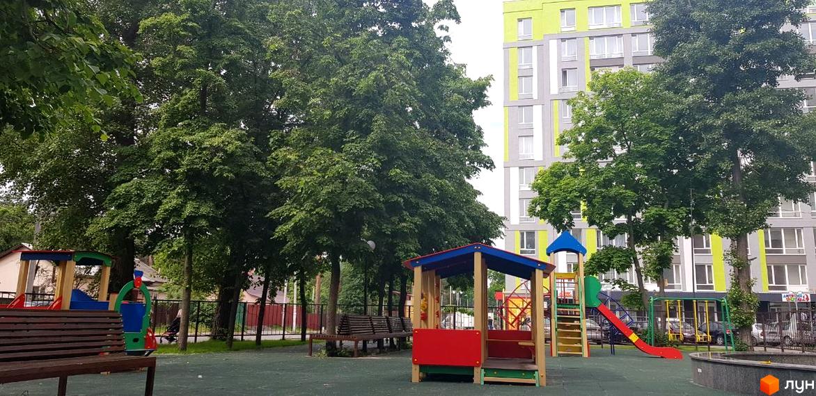 Житловий комплекс Lemongrass: багатоповерховий будинок з яскраво-зеленим фасадом, поруч дитячий майданчик з гірками та гойдалками, оточений деревами.
