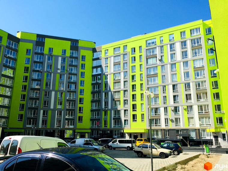 Житловий комплекс Lemongrass: багатоповерховий будинок яскравих кольорів (зелений, сірий) з численними вікнами. Перед ним розташований паркінг з автомобілями.