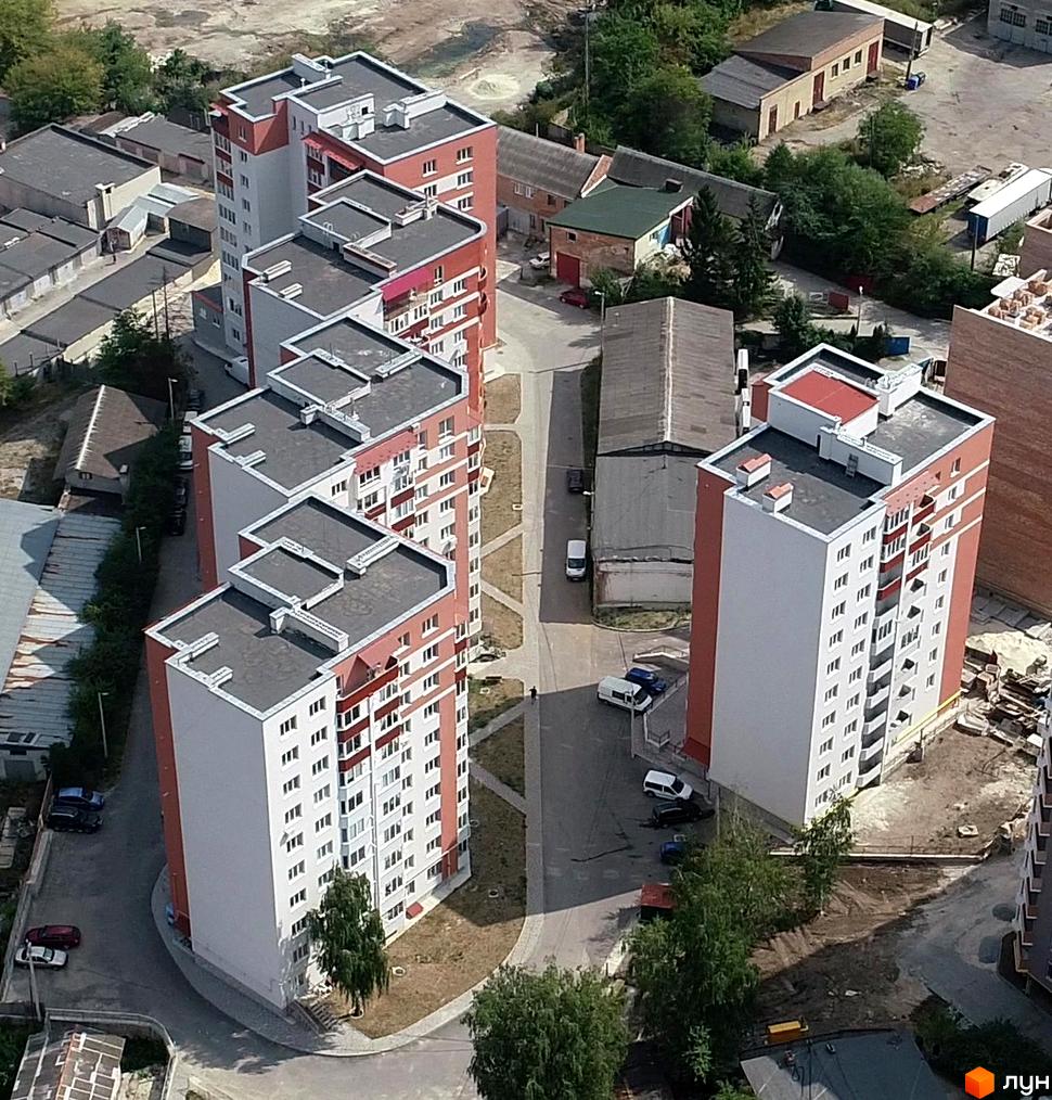 Зовнішній вигляд житлового комплексу на вул. Тролейбусна, 5. На зображенні видно багатоповерхові будинки з червоно-білими фасадами та прибудинкову територію з деревами та автомобілями.