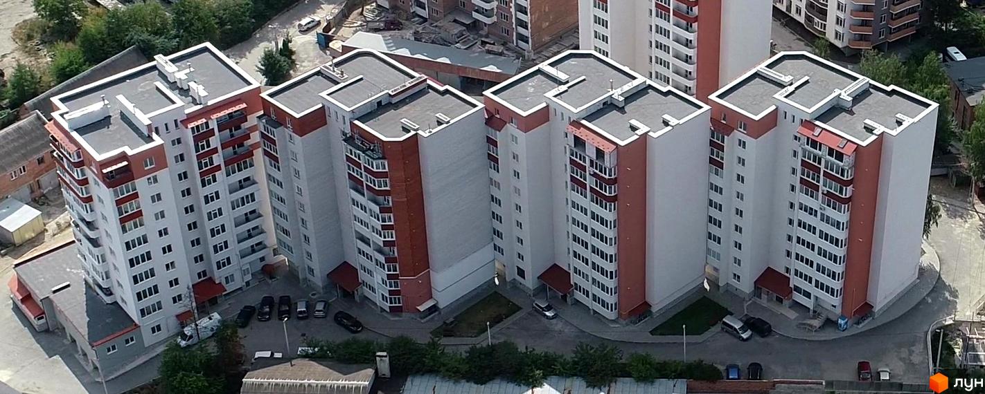 Зовнішній вигляд житлового комплексу на вулиці Тролейбусна, 5. Багатоповерхові будинки з червоно-білими фасадами та балконами. Прибудинкова територія з парковкою та зеленими насадженнями.
