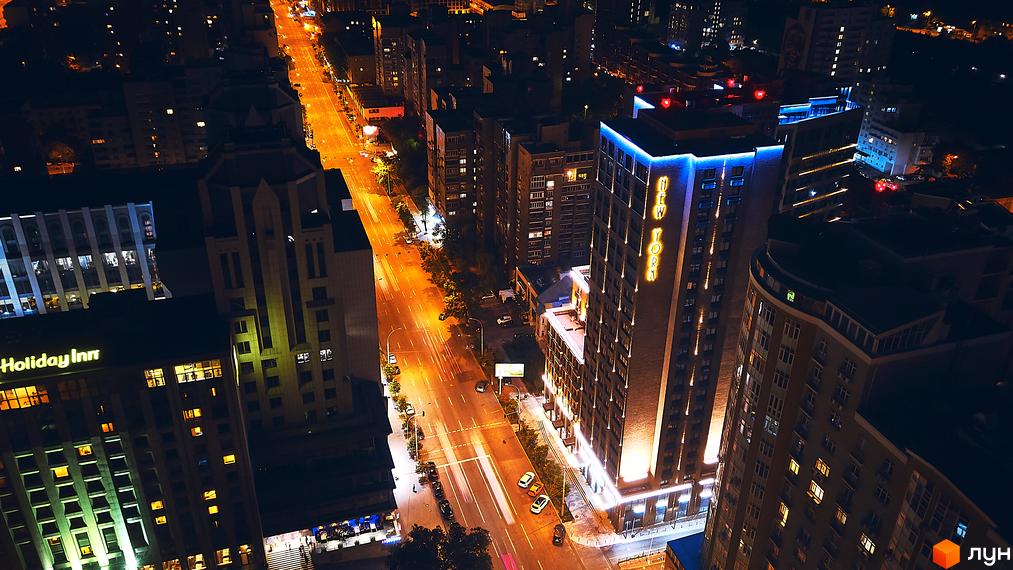 Вид з висоти на Житловий комплекс New York Concept House вночі. Висока будівля з підсвіткою та написом New York вздовж дороги.