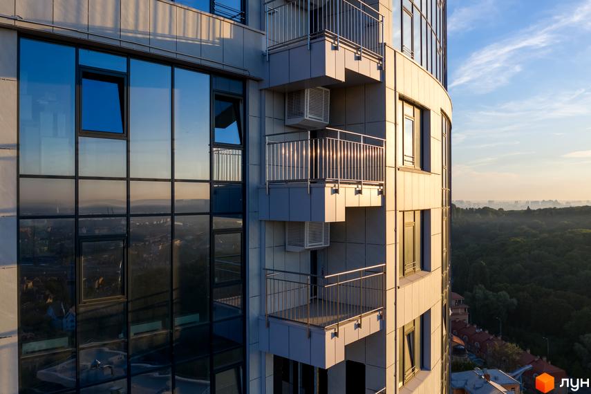 Екстер'єр житлового комплексу Busov Hill з панорамними вікнами та балконами. Вид на зелене місто на заході сонця.
