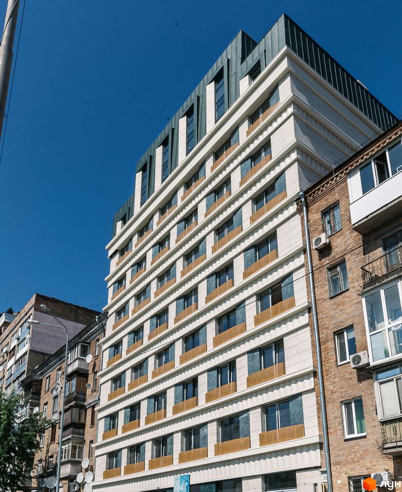 Житловий комплекс Einstein Concept House – новобудова зі світлим фасадом, темними вікнами та металевим дахом. Розташована поруч із цегляною спорудою.