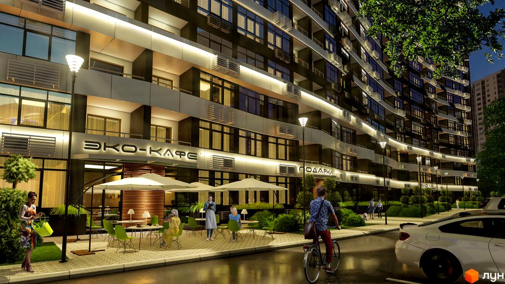 Вигляд фасаду будівлі житлового комплексу Атмосфера з кафе та зоною відпочинку. На вулиці припарковані авто та їздить велосипедист.