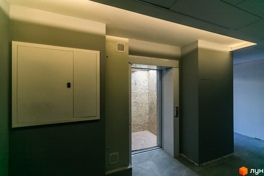 Інтер'єр коридору Житлового комплексу Einstein Concept House: відкритий ліфт з дерев'яною обшивкою та технічна шафа на стіні.
