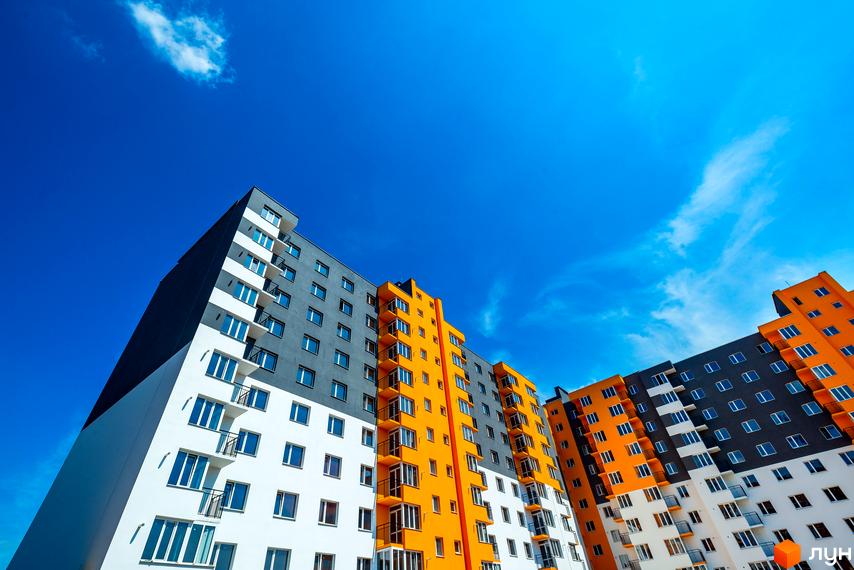 Новобудова ЖК Сімейний COMFORT з яскравим фасадом та балконами на тлі блакитного неба. Зовнішній вигляд будинку з білими, сірими та помаранчевими елементами.