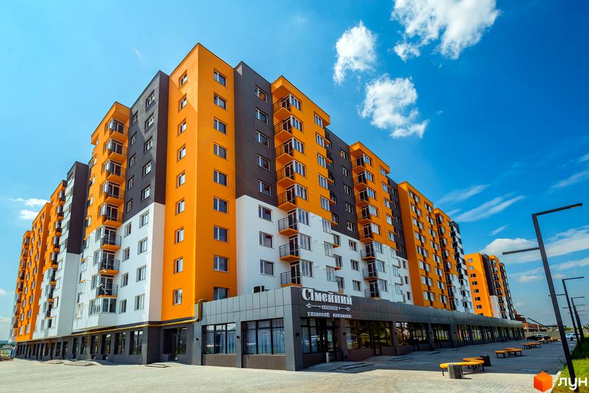 Житловий комплекс Сімейний COMFORT з яскравим фасадом у помаранчевих, сірих та білих тонах. На території комплексу розташовані лавки та ліхтарі.