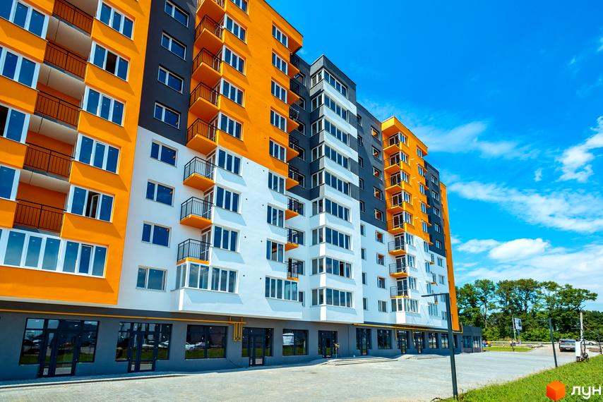 Житловий комплекс Сімейний COMFORT - яскрава новобудова з жовтими та білими фасадами, балконами та великими вікнами. Поруч асфальтована дорога та зелена зона.