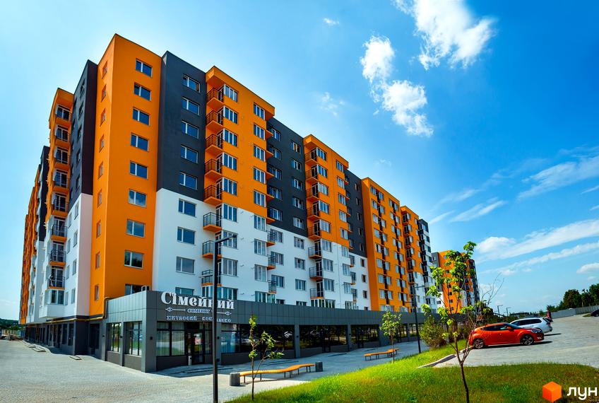Житловий комплекс Сімейний COMFORT – яскрава новобудова з білими, сірими та помаранчевими фасадами. Біля будинку облаштована прибудинкова територія з зеленими насадженнями та парковкою.