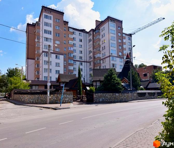 Зображення багатоповерхового будинку на вулиці Целевича, 4а. На передньому плані видно дорогу та частину прибудинкової території з кам'яною огорожею.