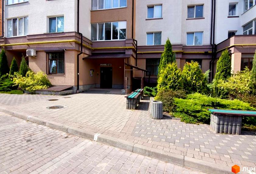 Зовнішній вигляд будинку на Целевича, 4а. Прибудинкова територія з лавками та зеленими насадженнями.