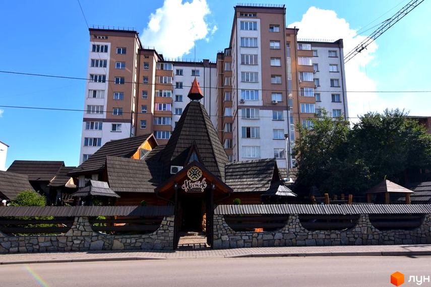 Зовнішній вигляд будинку на Целевича, 4а. Багатоповерхівка з великими вікнами та дерев'яним оздобленням фасаду.