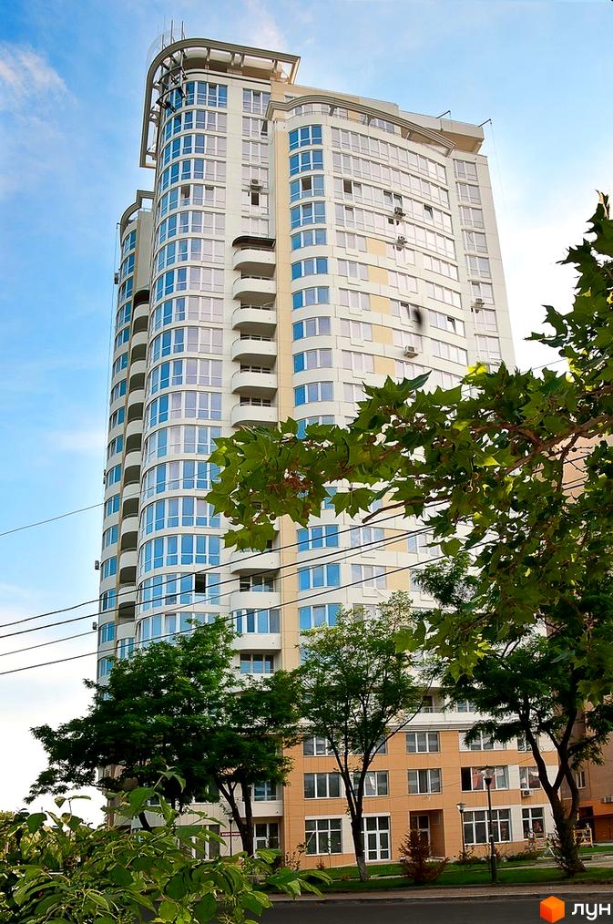 Житловий комплекс Руслан і Людмила з великими вікнами та балконами. Прибудинкова територія озеленена деревами та кущами.