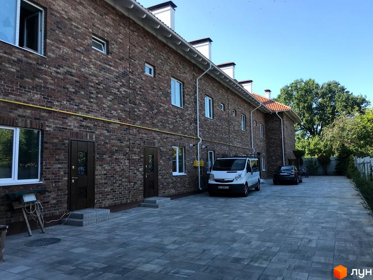 Таунхауси „На Достоєвського“ – цегляні будинки з червоної цегли з білими вікнами та дахами. Перед будинками облаштований паркінг з бруківкою та зелені насадження.